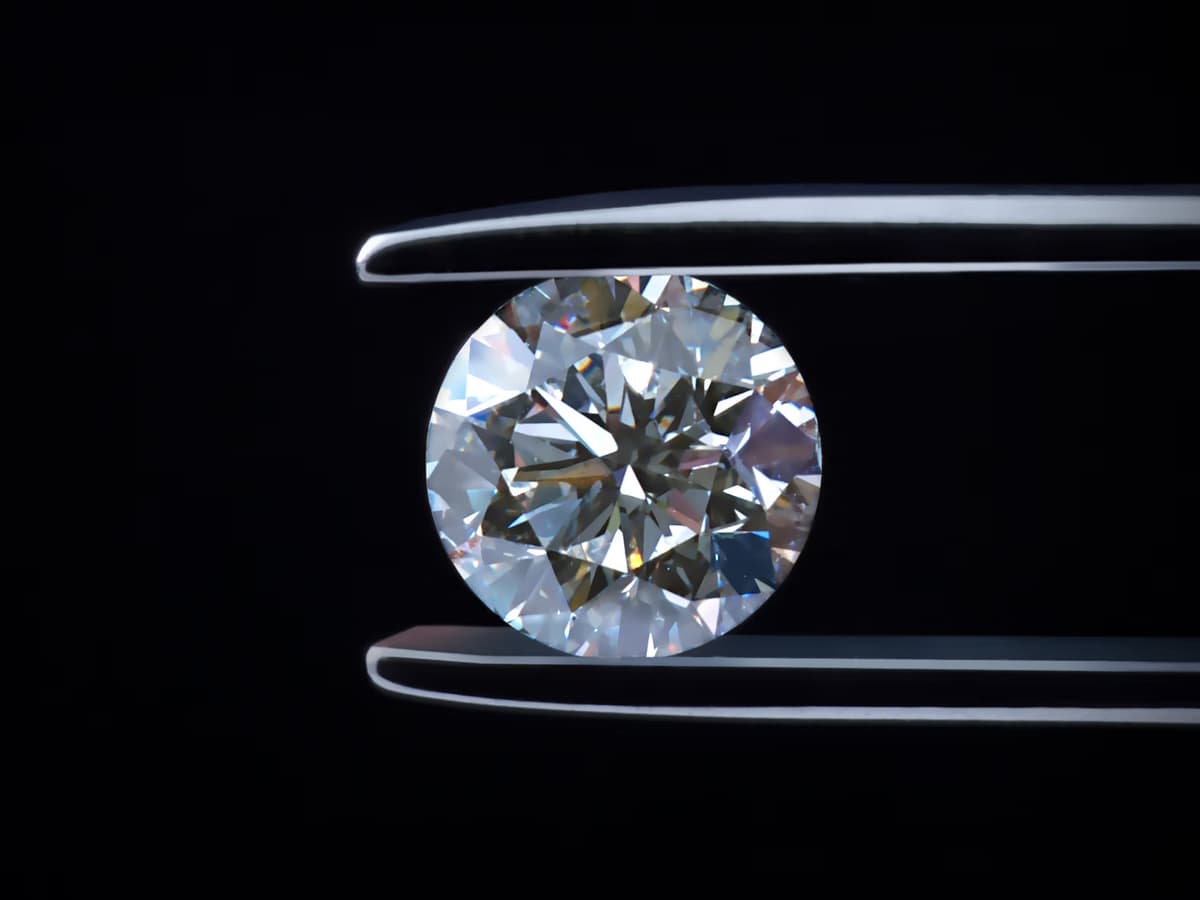 A round brilliant held in tweezers against black, the way a stone is examined before it is graded
