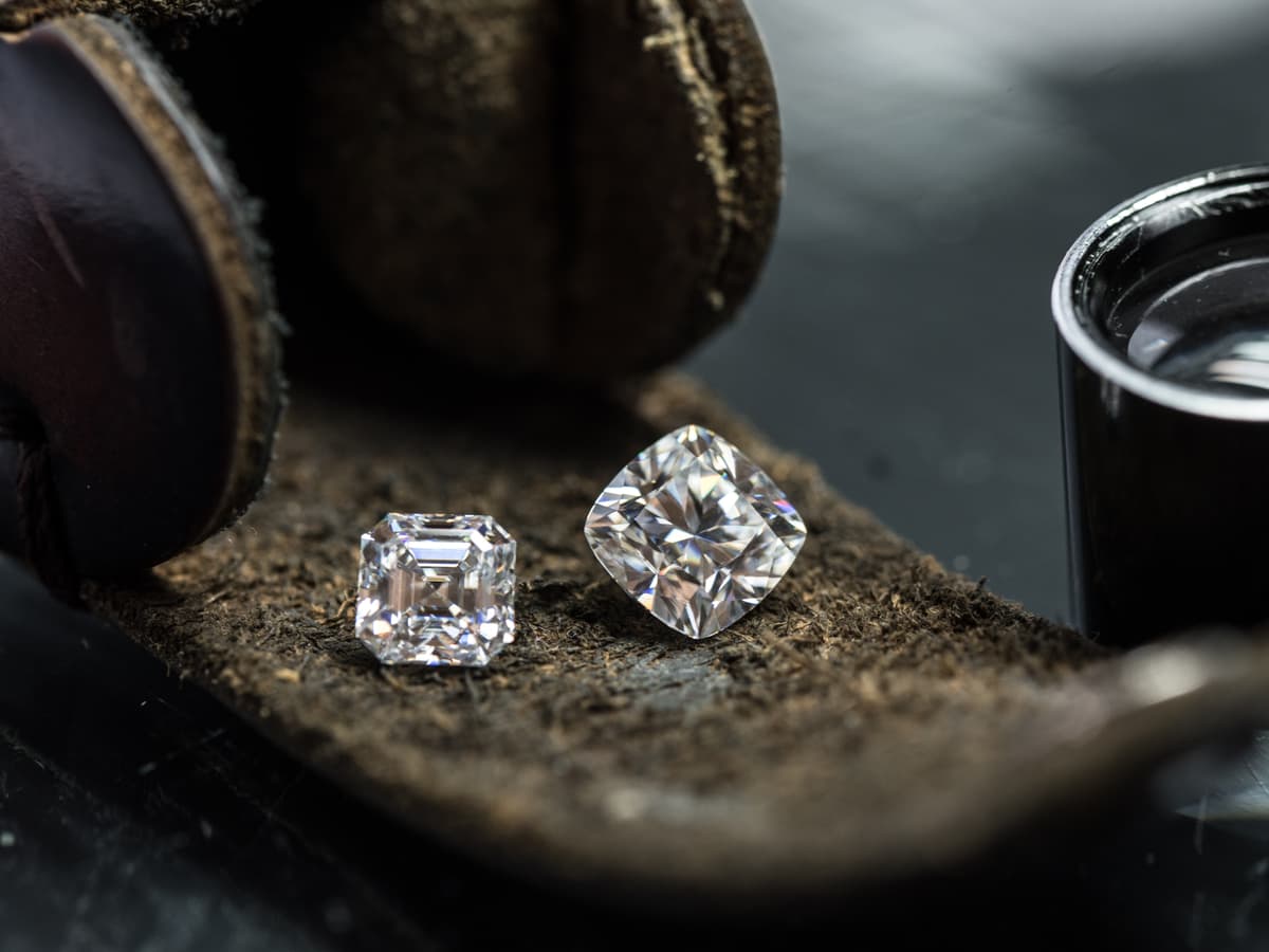 Two step cut diamonds resting on a worn leather parcel pad beside a jeweler’s loupe