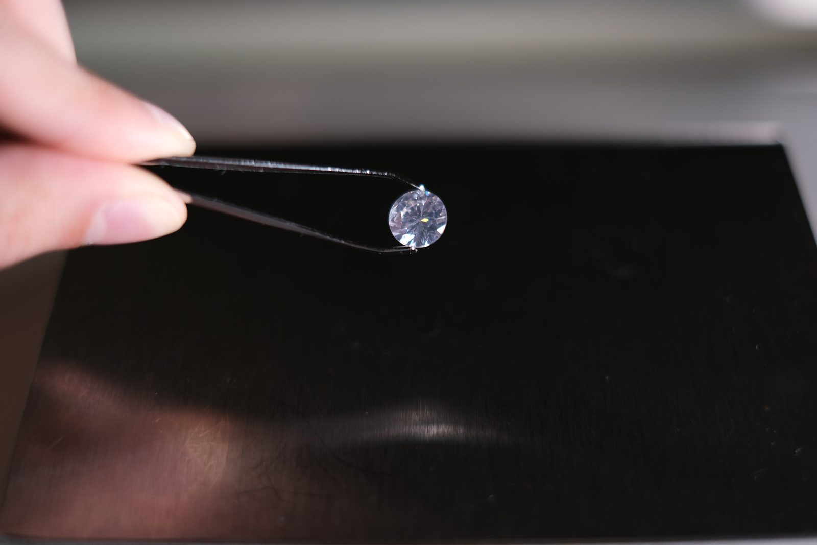 A loose round diamond held in tweezers over a dark background for inspection