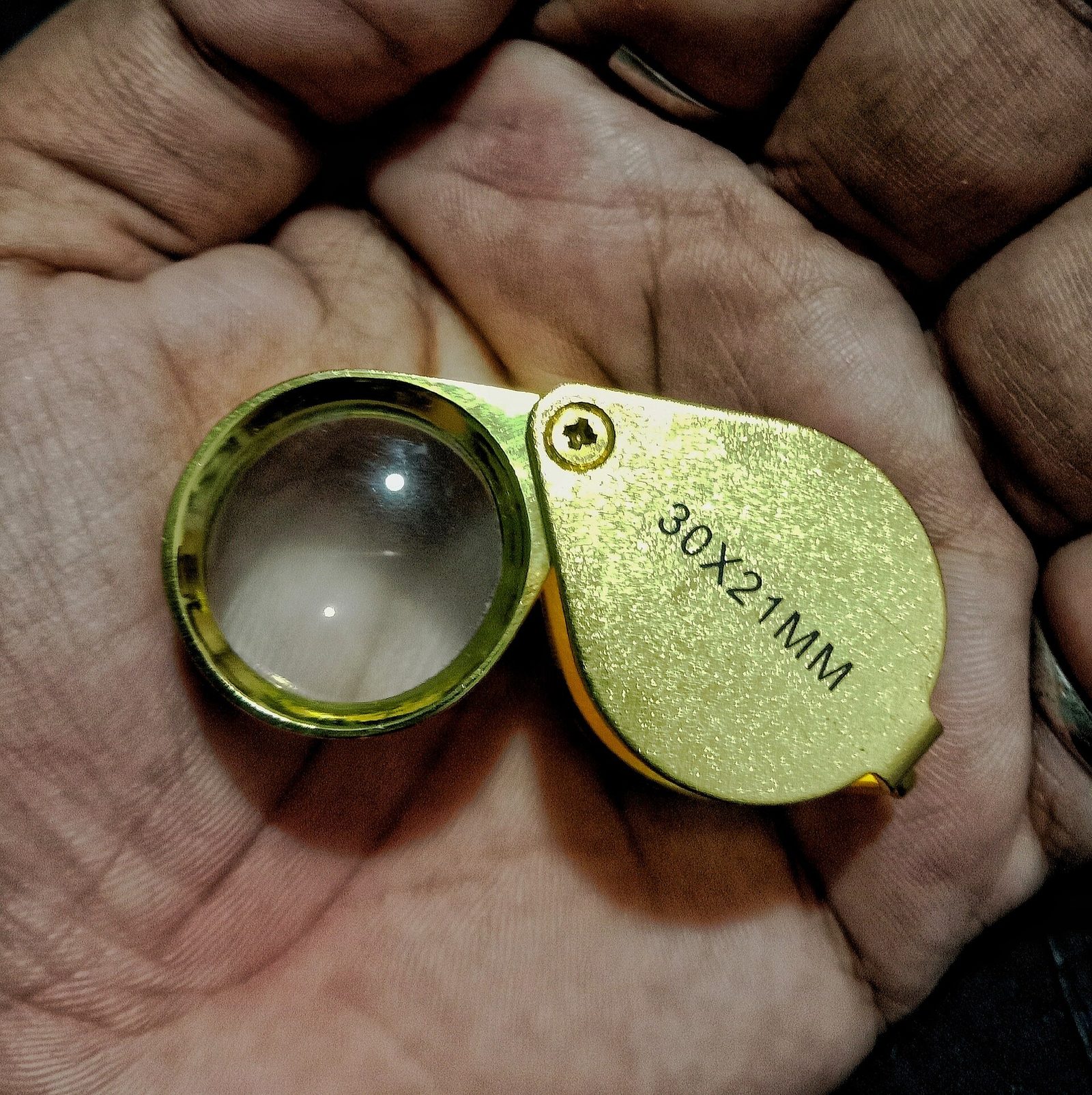 A gold toned jeweler's loupe held open in a hand, the magnifying lens used to check a stone against the numbers printed on its report